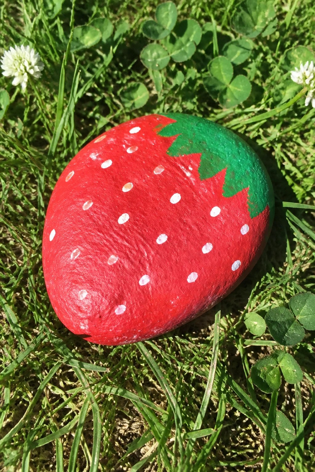 Painted red strawberry rock with white dots and green leaves on grass