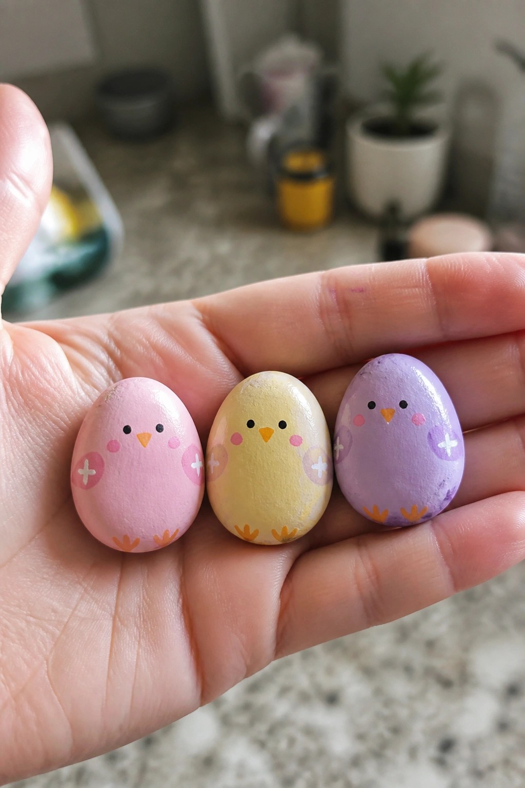 Hand holding three pastel chick eggs painted pink, yellow, and purple.
