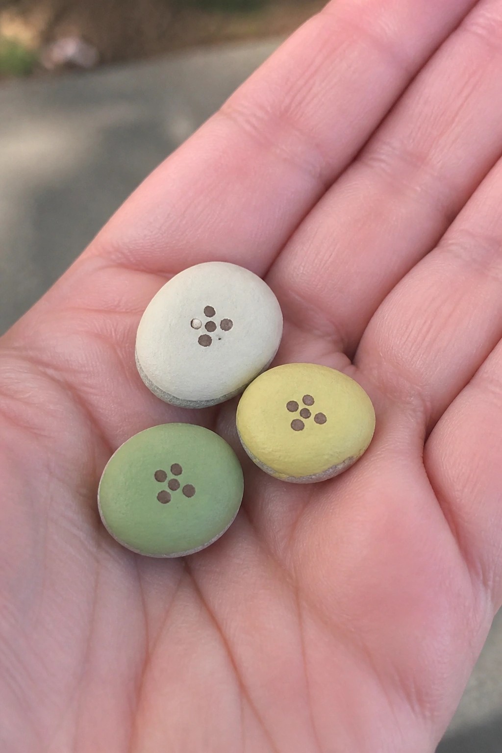 Open palm holding three small round buttons painted white, yellow, and green.
