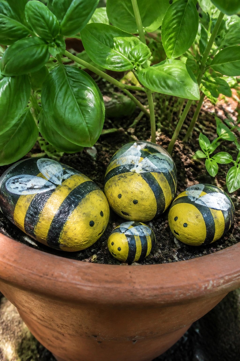 Four yellow-and-black painted bee rocks in a leafy terracotta pot