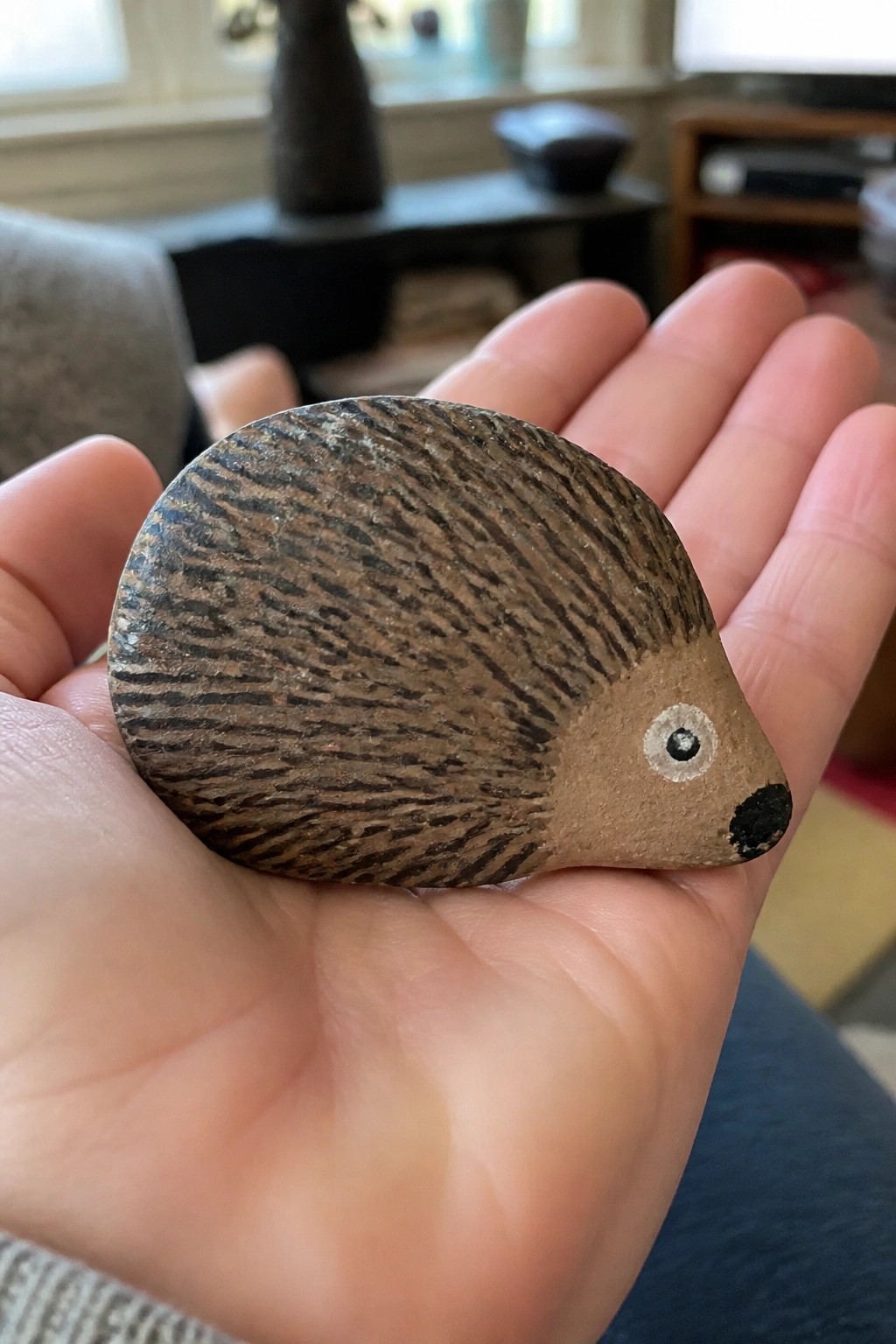 Hand holding painted stone hedgehog with brown striped quills, black nose and white eye.