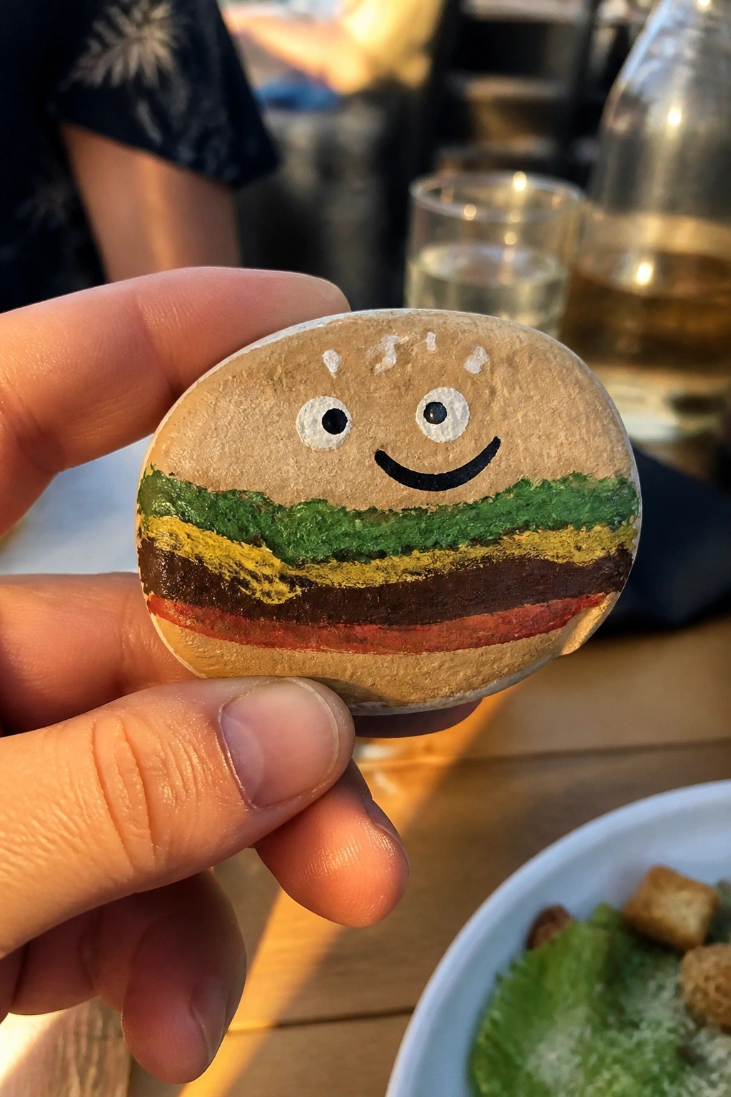 Hand holding smiling hamburger rock with green, yellow, and red layers