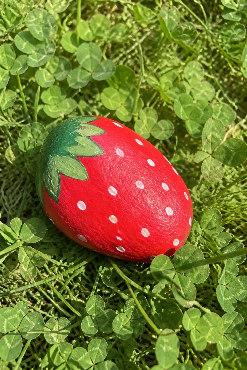 Red strawberry-painted egg with green leaves and white dots on clover grass