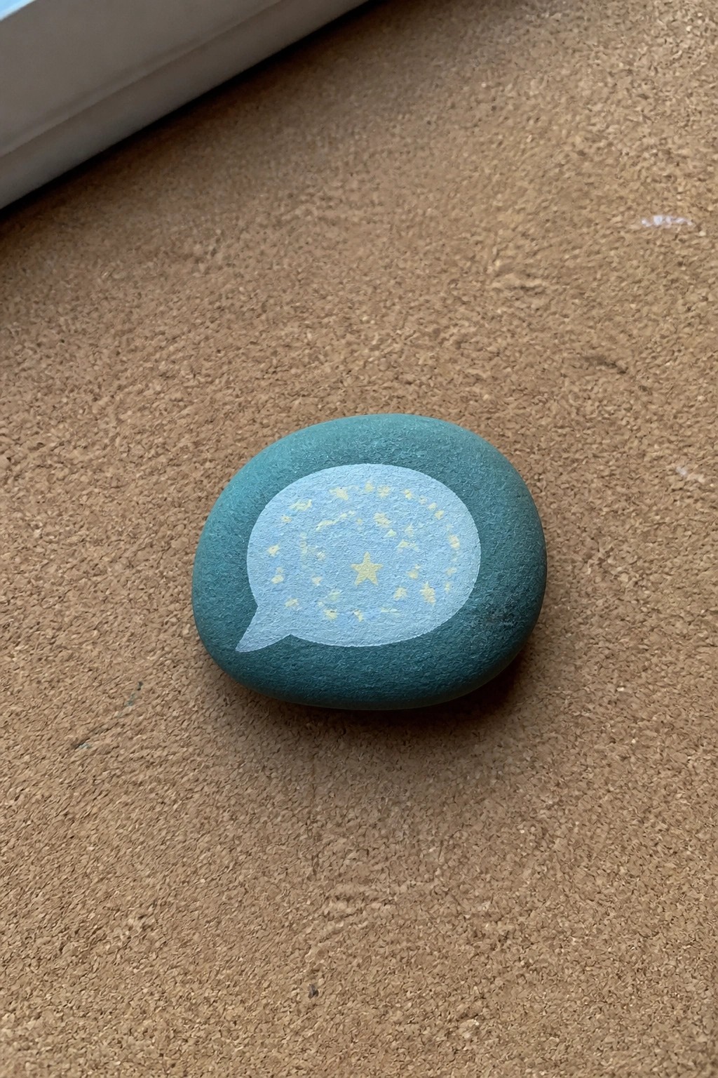 Teal stone with light blue speech bubble and yellow stars on brown surface.