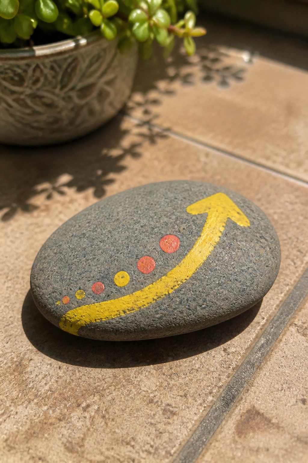 Gray stone with yellow arrow and red-yellow dotted trail on tiled floor near plant