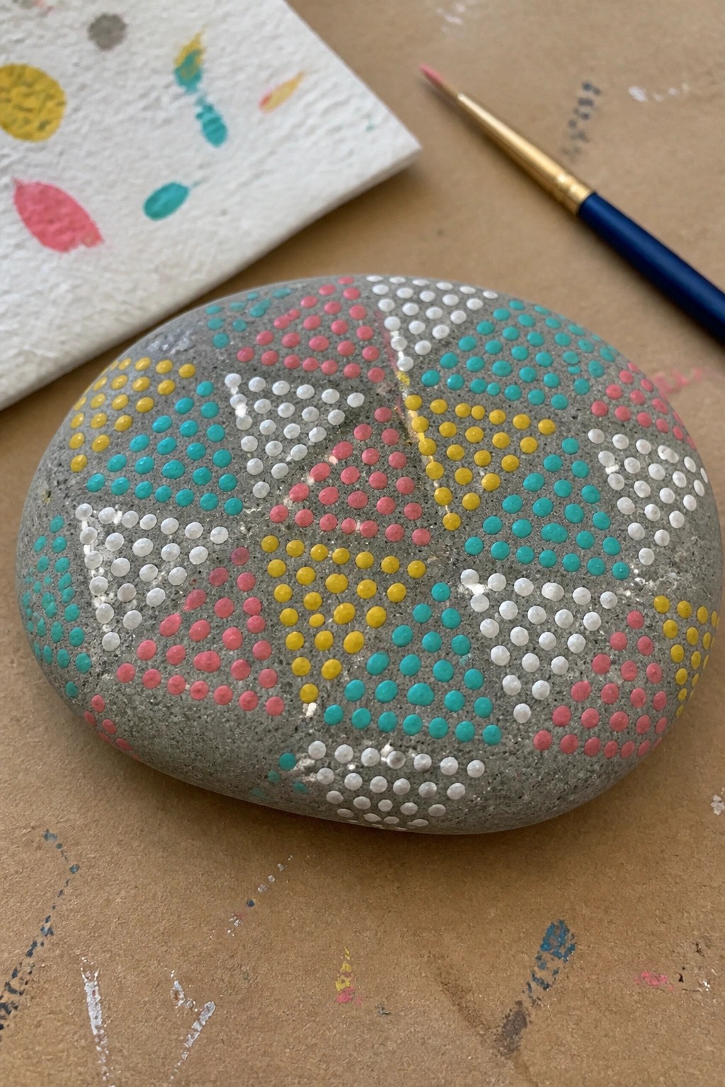 Gray stone with yellow, pink, turquoise, and white dotted patterns beside paintbrush.