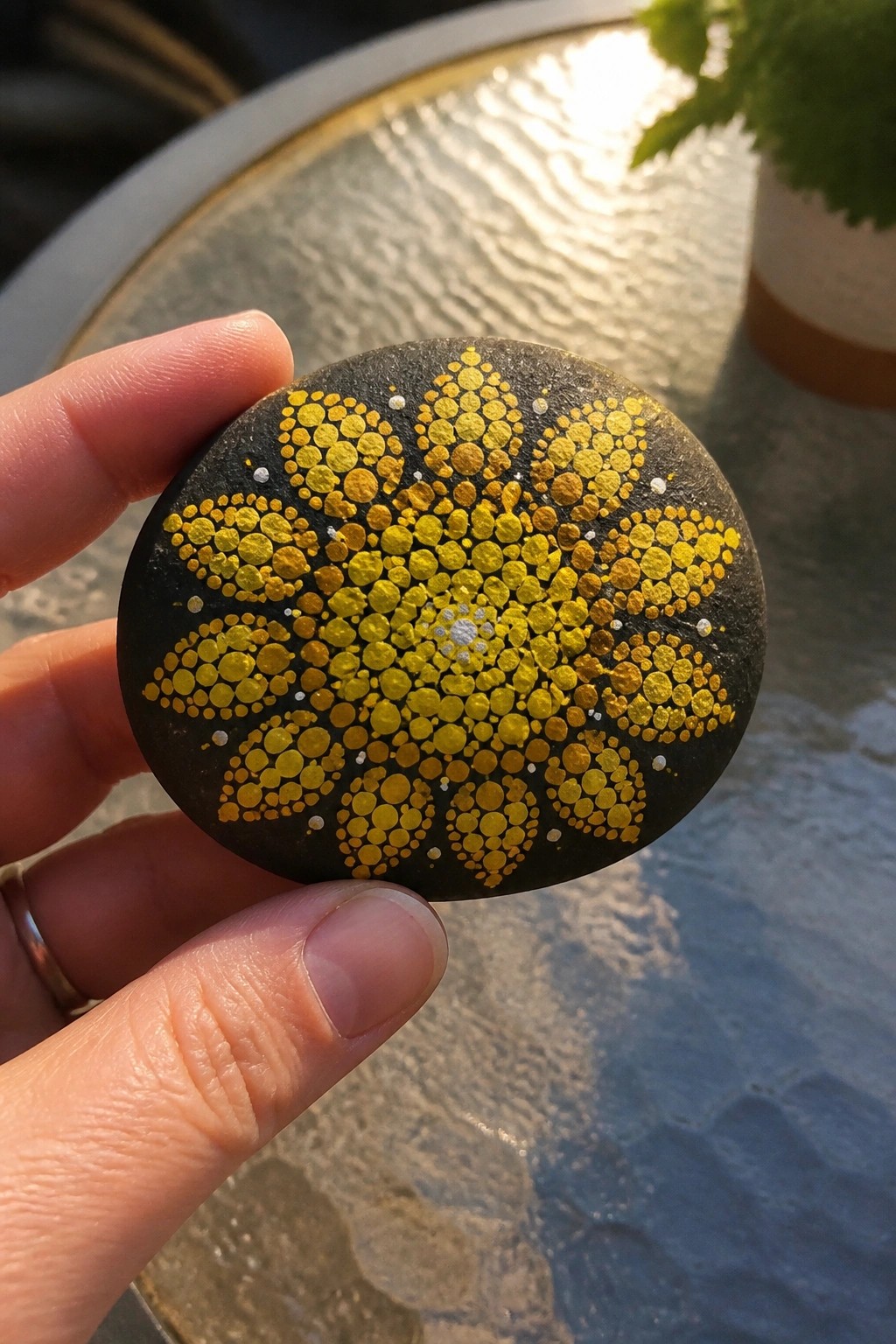 Hand holding black stone with yellow gold dotted flower mandala design