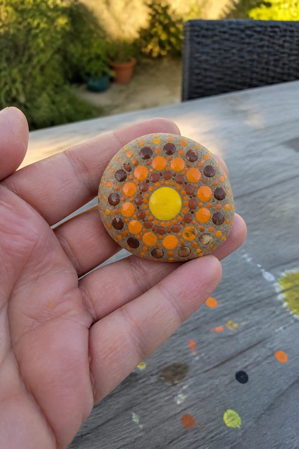 Hand holding round stone with yellow orange brown dot pattern circles