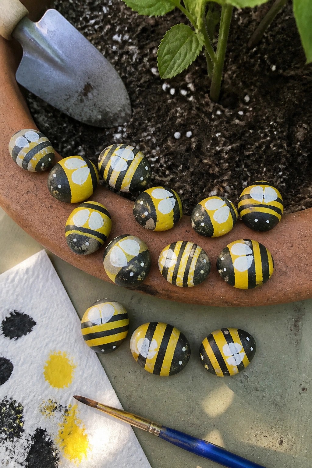 Painted bumblebee rocks on terracotta pot with trowel, brush, and paint palette