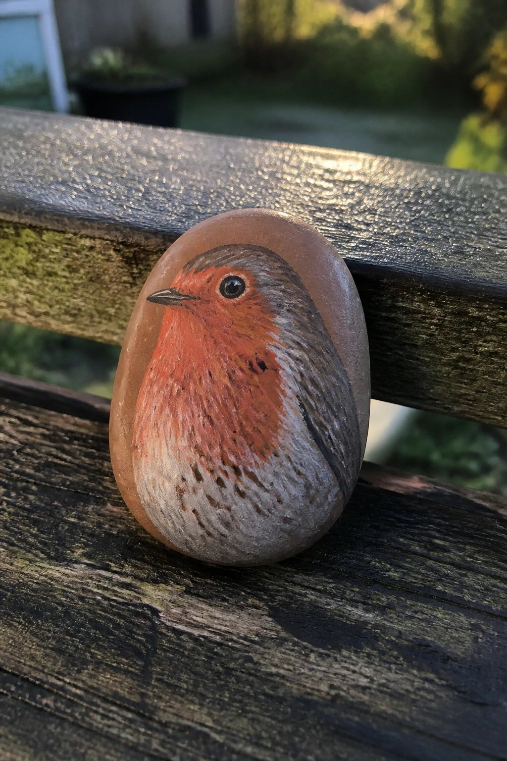 Painted robin with orange breast on oval stone atop wooden bench