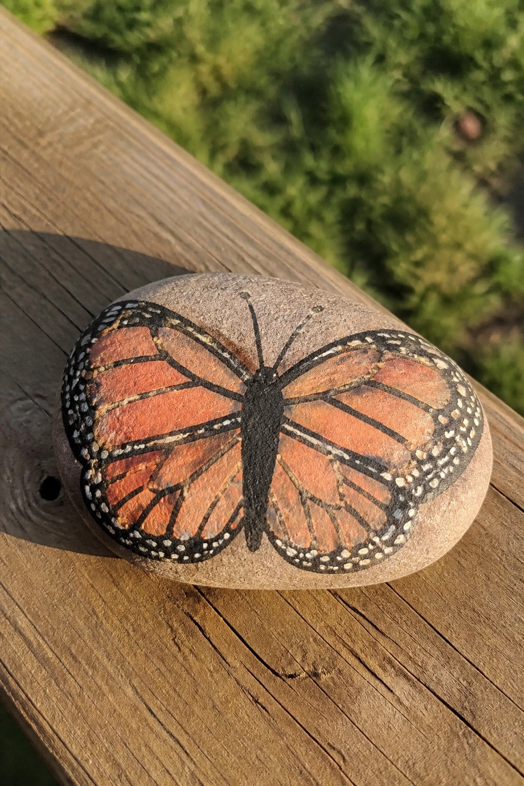Oval rock painted with orange monarch butterfly and black markings on wood