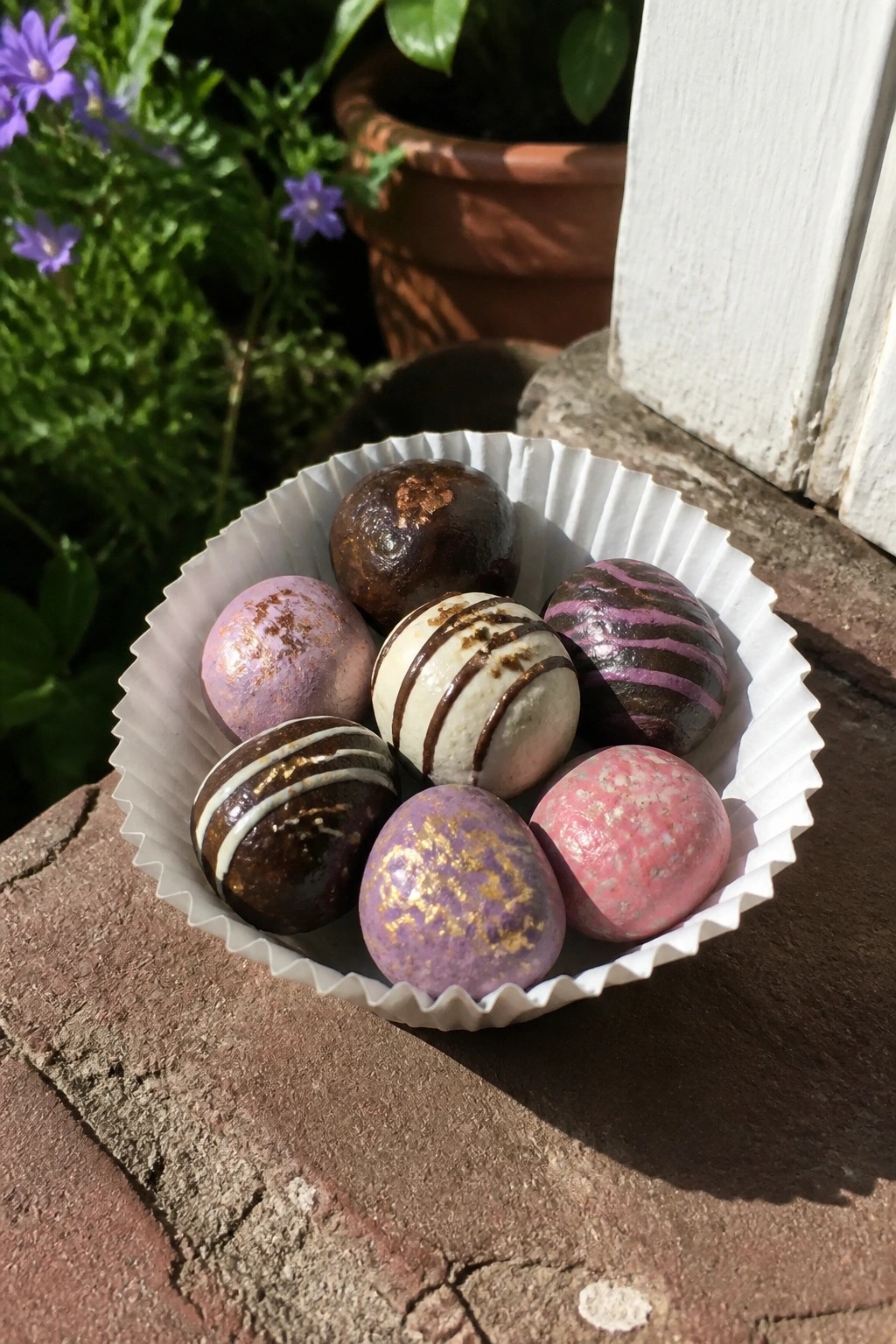 Assorted colorful chocolate truffles in a white paper liner on a brick surface