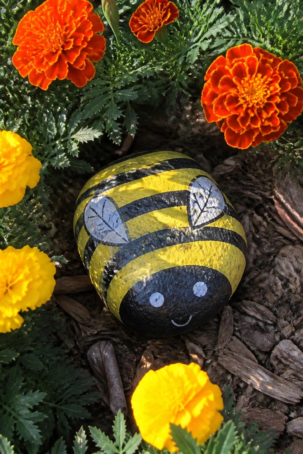 Painted yellow-and-black striped bee rock with wings among orange marigolds