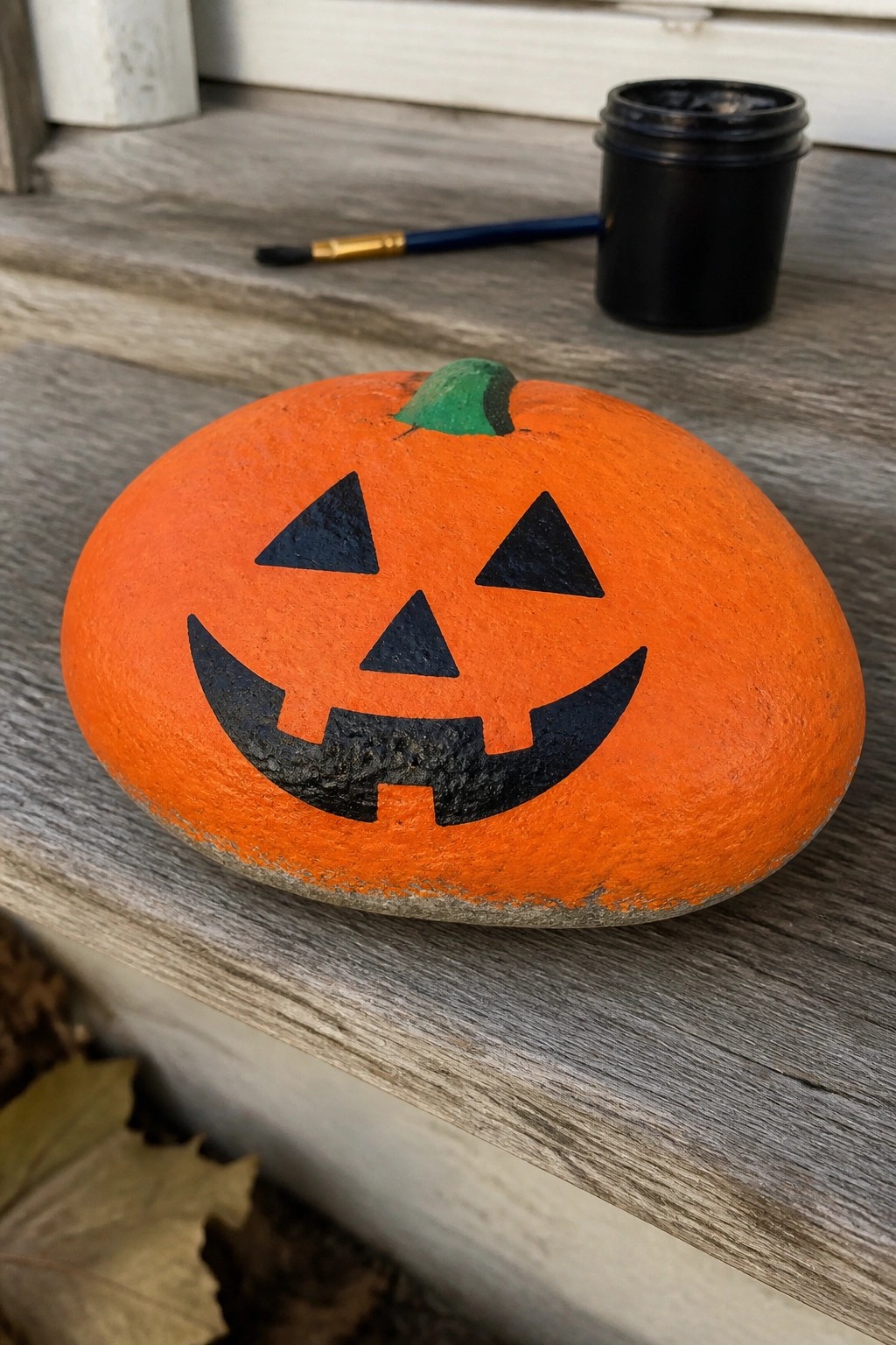 Orange rock painted as jack-o'-lantern with black face and green stem on wooden steps