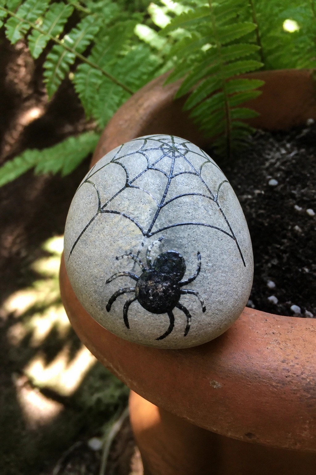 Gray stone painted with black spider and web on terracotta pot rim