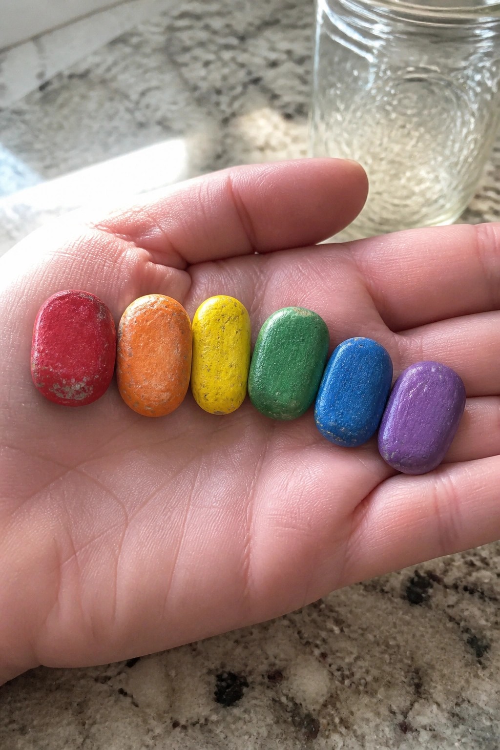 Hand holding six oval stones painted red, orange, yellow, green, blue, purple