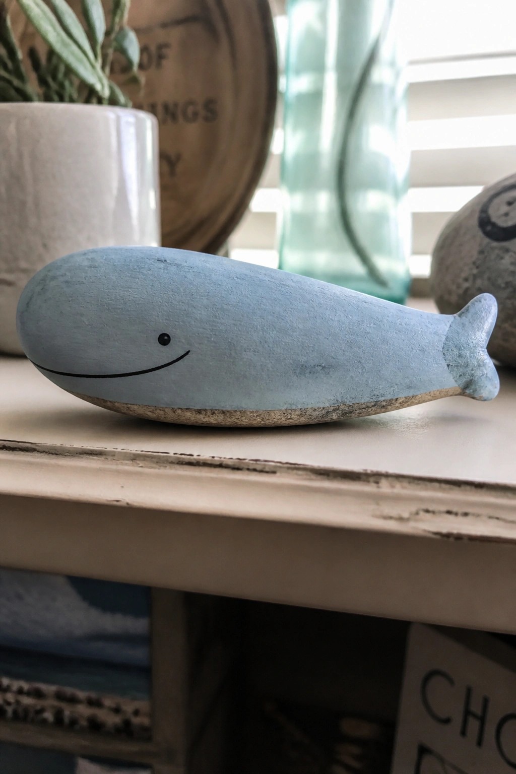Light blue wooden whale figurine with smiling face on white table