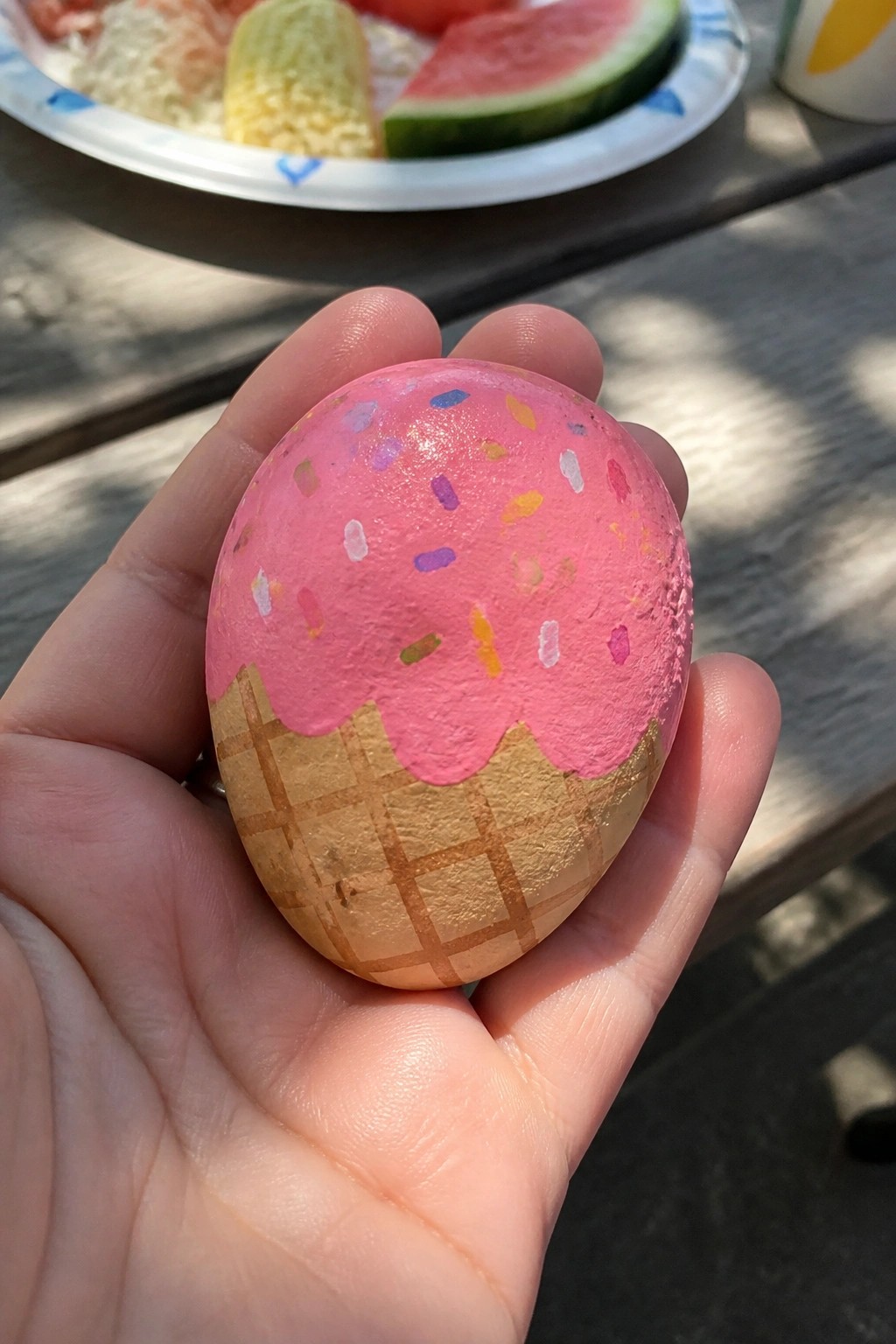 Hand holding egg painted as pink ice cream cone with sprinkles on waffle base