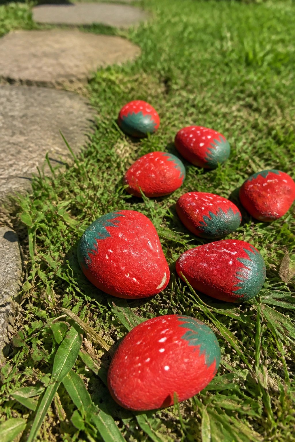 Painted rocks resembling strawberries scattered on green grass near stone steps.