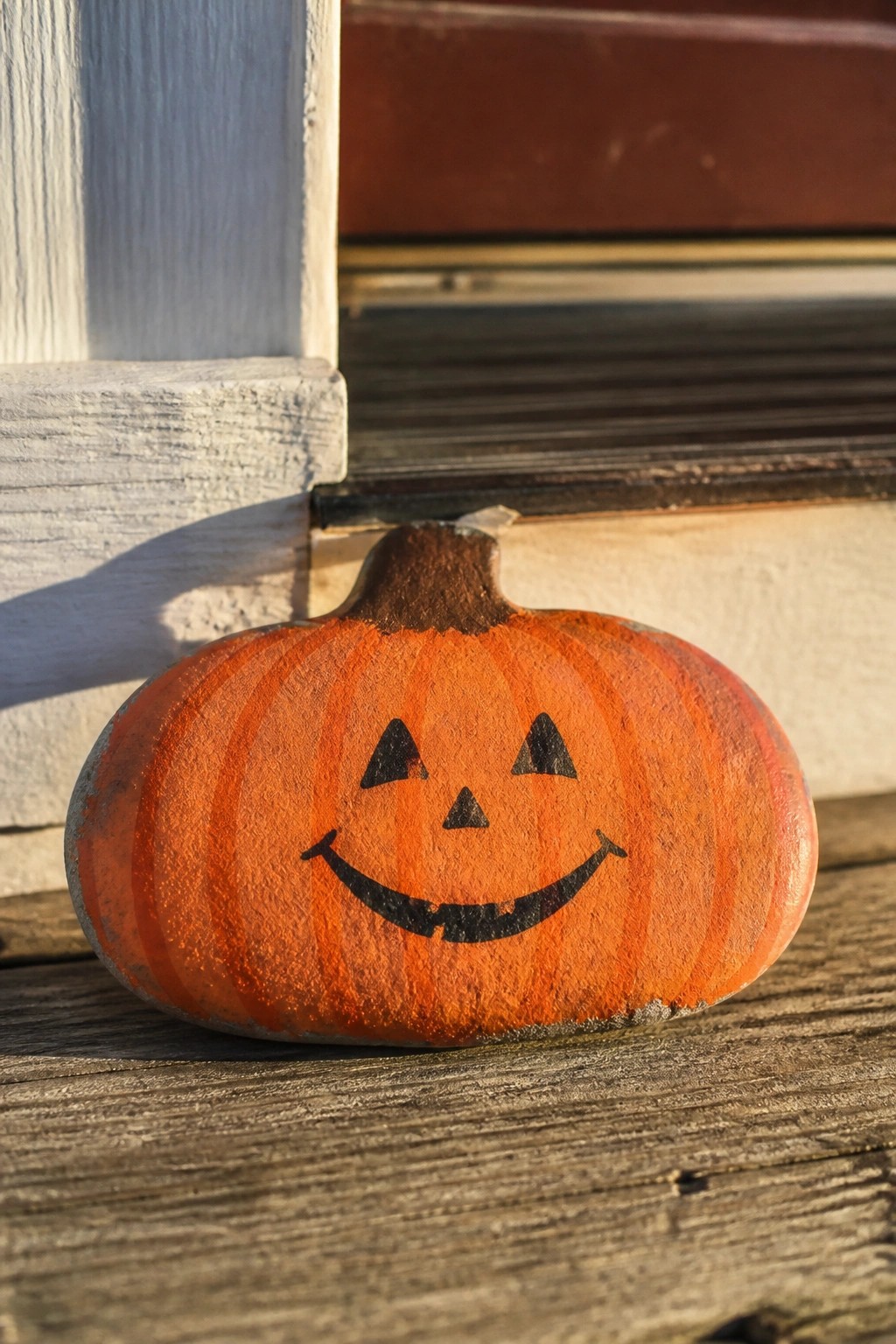 Small orange pumpkin with smiling jack-o'-lantern face on wooden porch steps