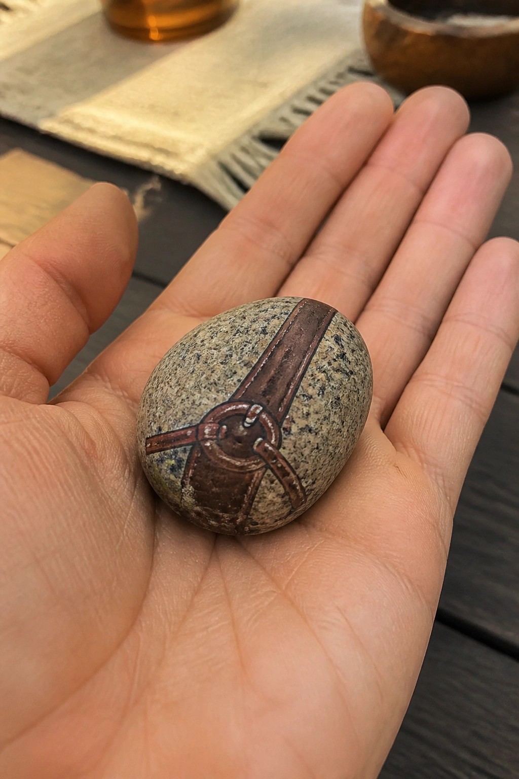 Hand holding speckled stone painted with brown leather strap and buckle design