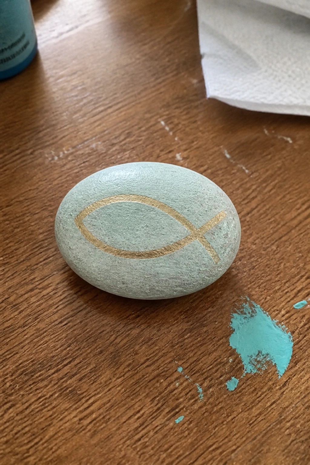 Light green painted stone with gold fish symbol on wood beside paint smear