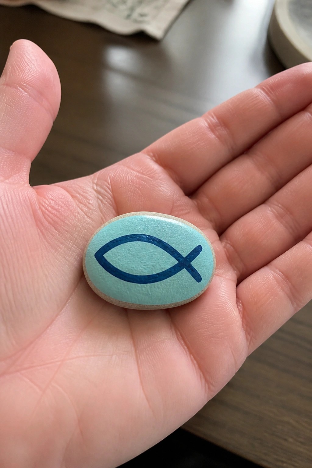Open hand holding turquoise oval stone painted with blue fish symbol