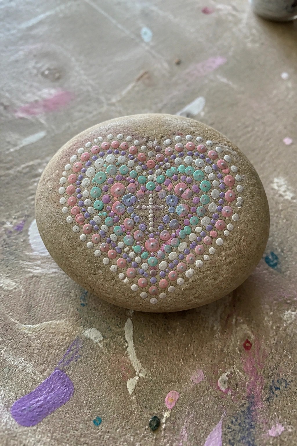 Round beige stone with pastel dotted heart on paint-splattered surface