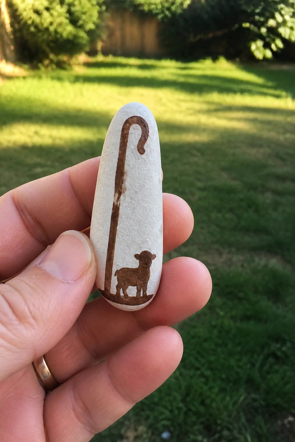 Hand holding white stone painted with brown shepherd's crook and lamb