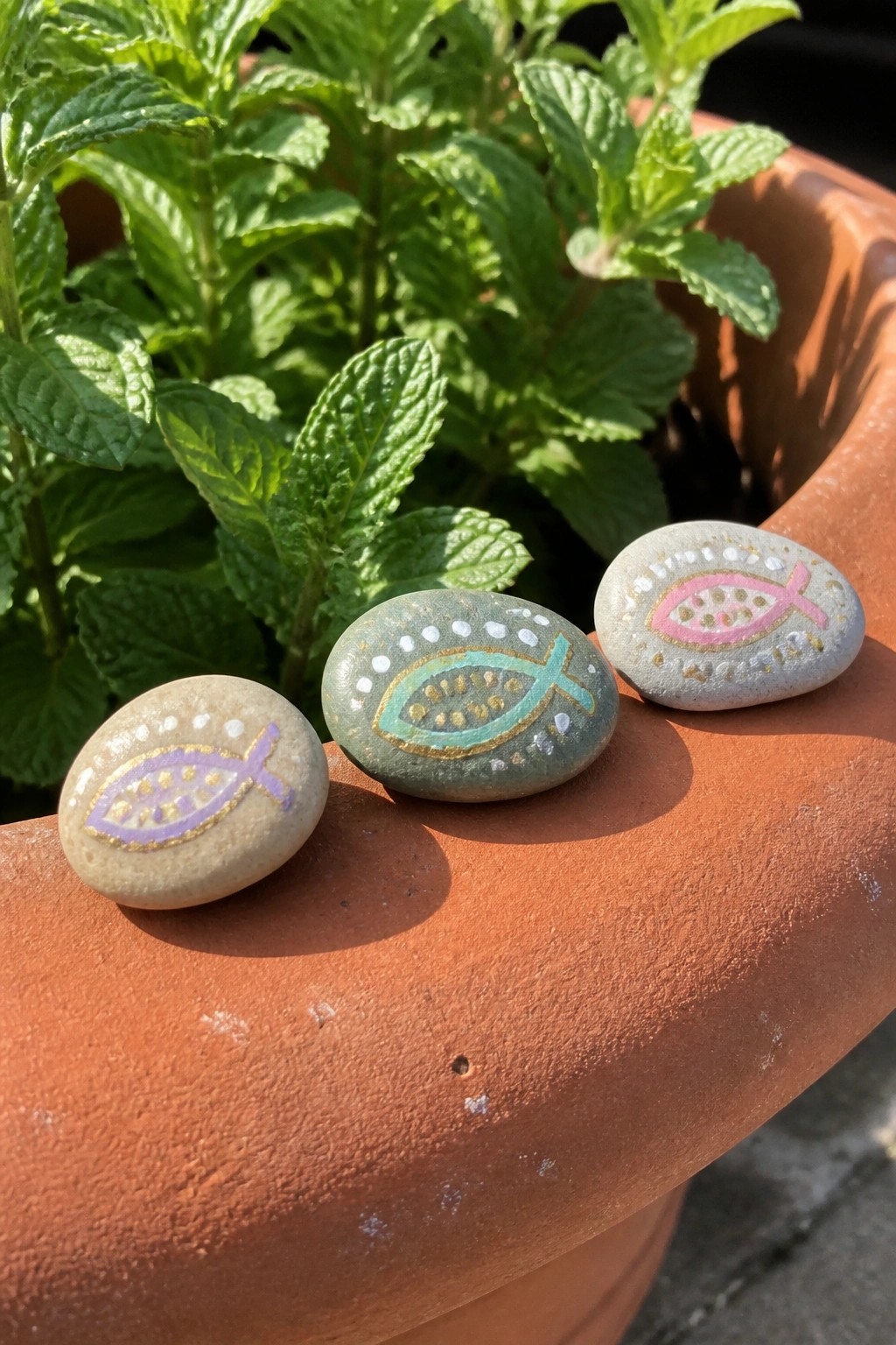 Three colorful fish symbols painted on stones atop terracotta pot edge