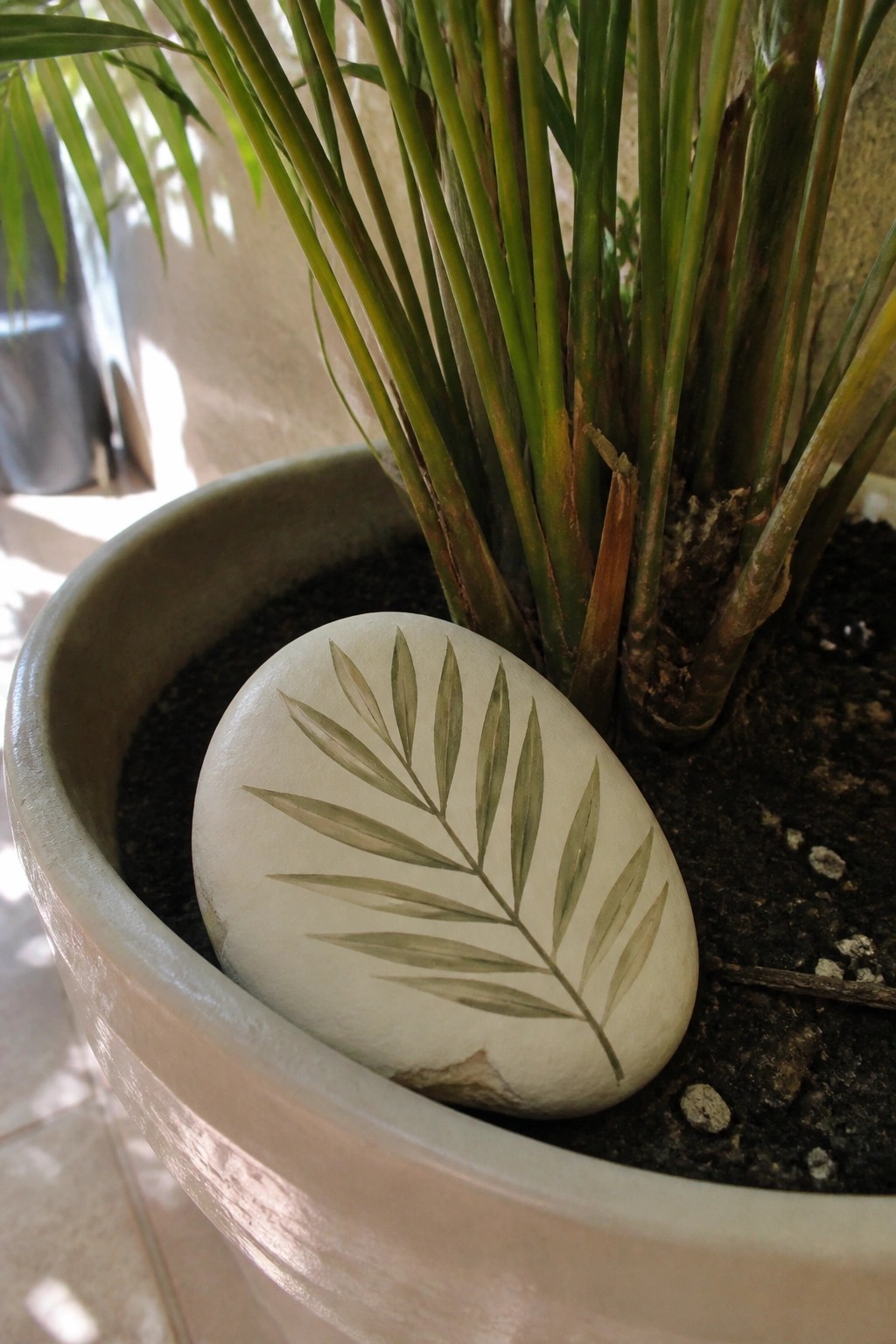 White stone with green leaf painting resting in potted plant soil