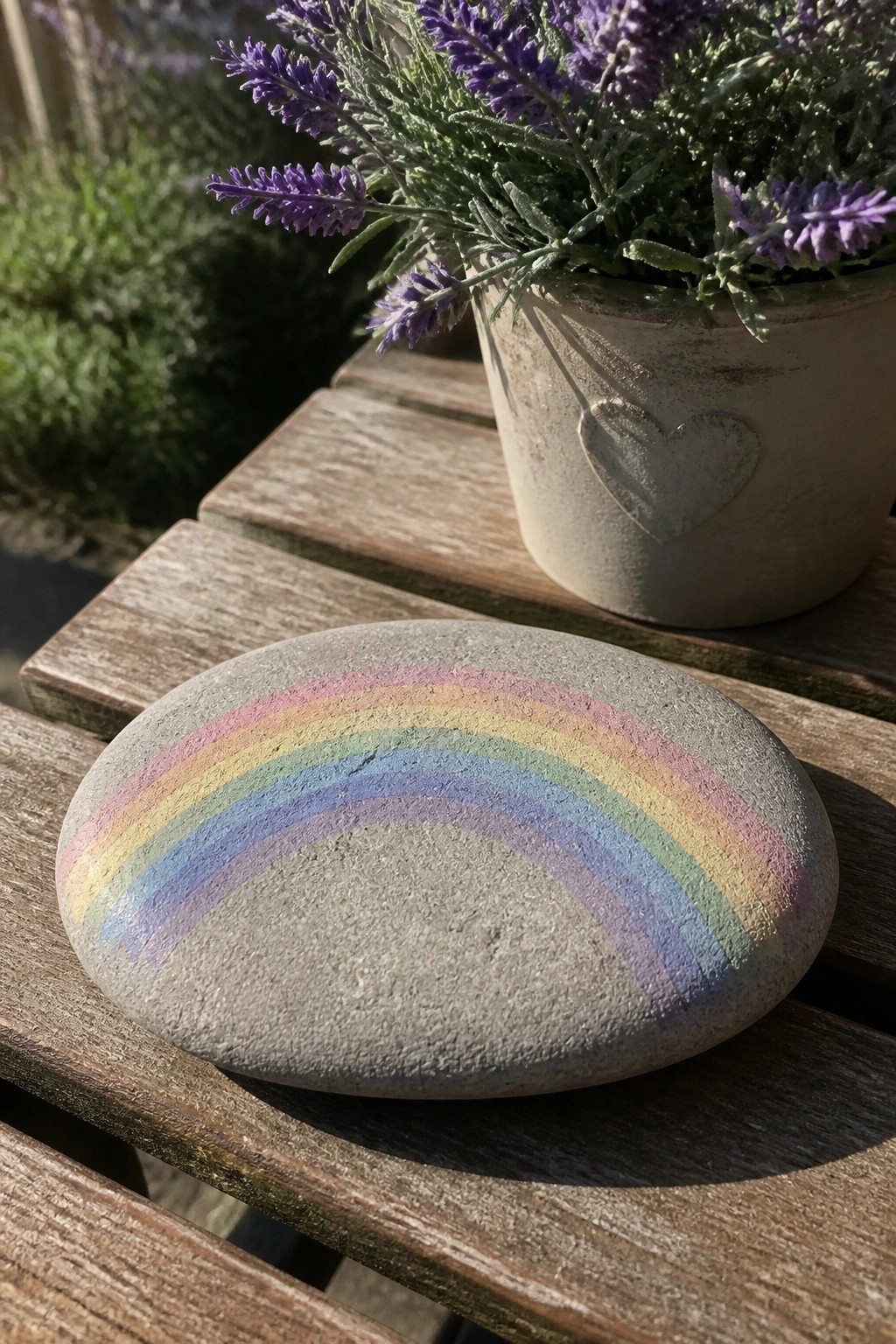 Rainbow-painted stone on wooden table beside potted purple lavender in heart pot