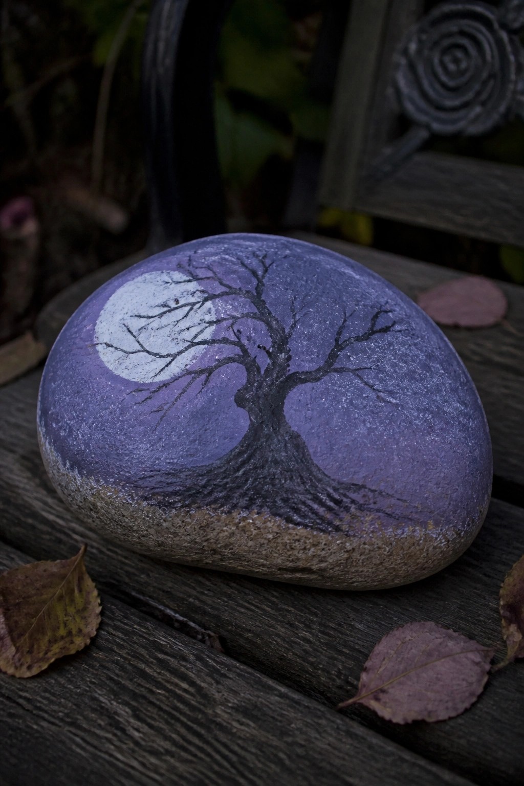 Painted rock with bare tree silhouette and full moon against purple sky