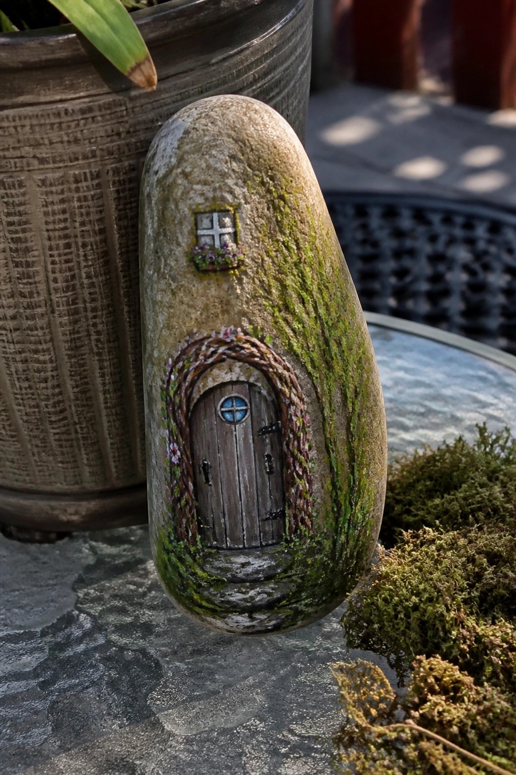 Painted stone with miniature wooden door, vine archway, moss, and tiny window.
