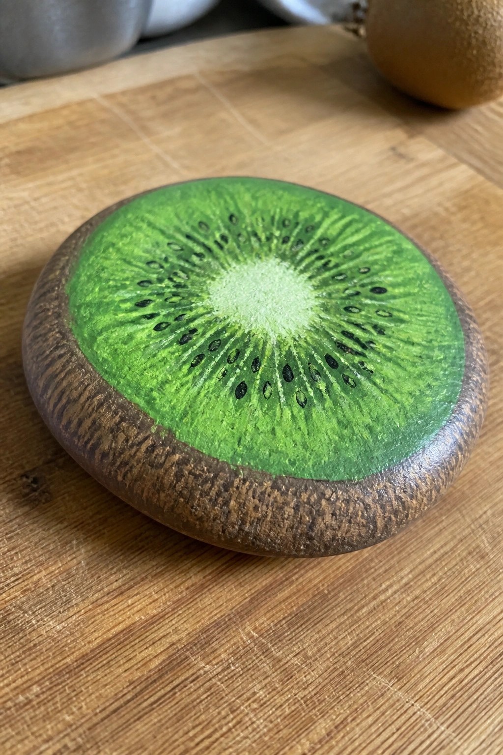 Painted round object showing vibrant green kiwi slice with seeds on wood
