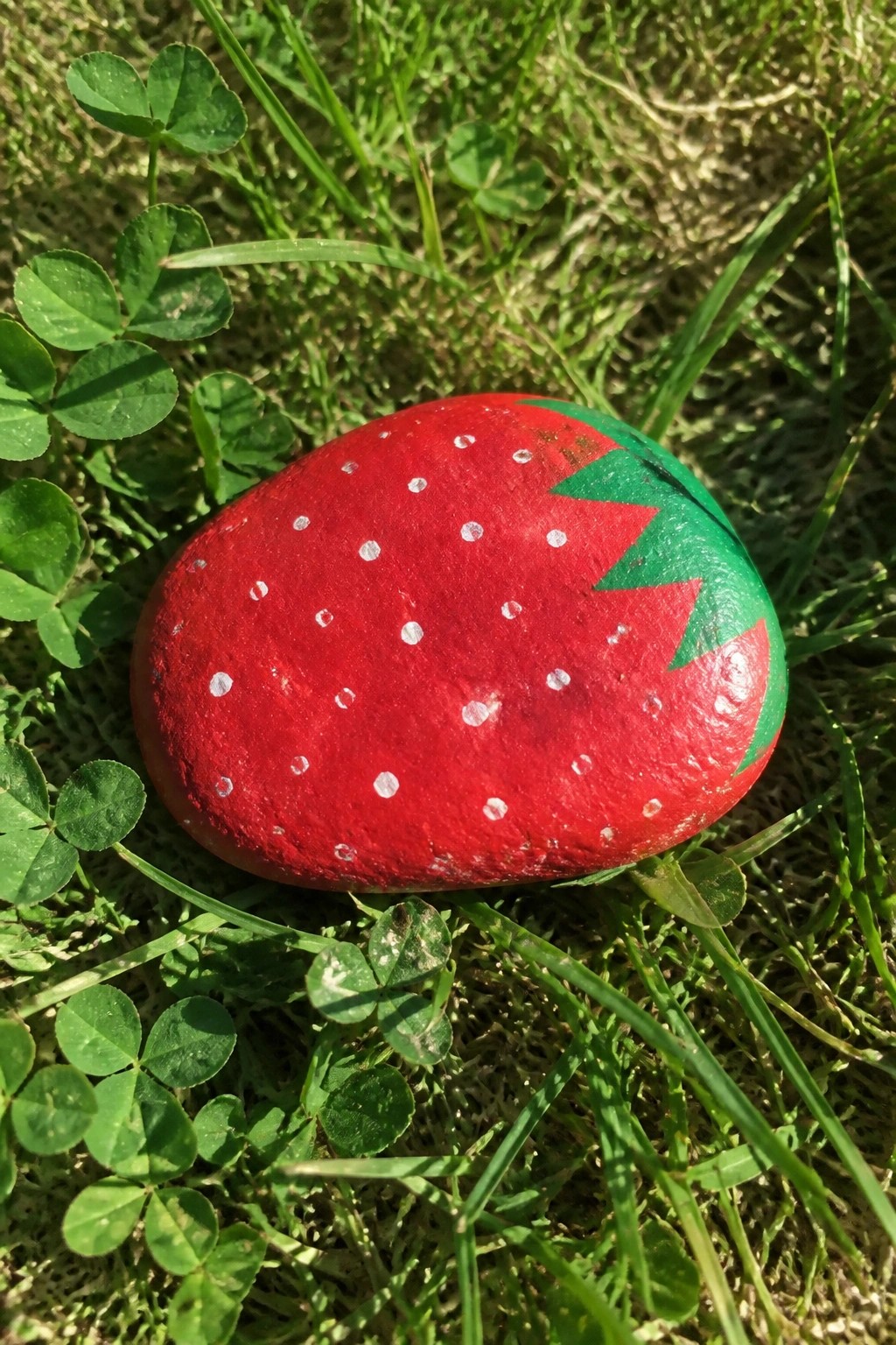 Red painted rock as strawberry with white dots and green leaves on grass