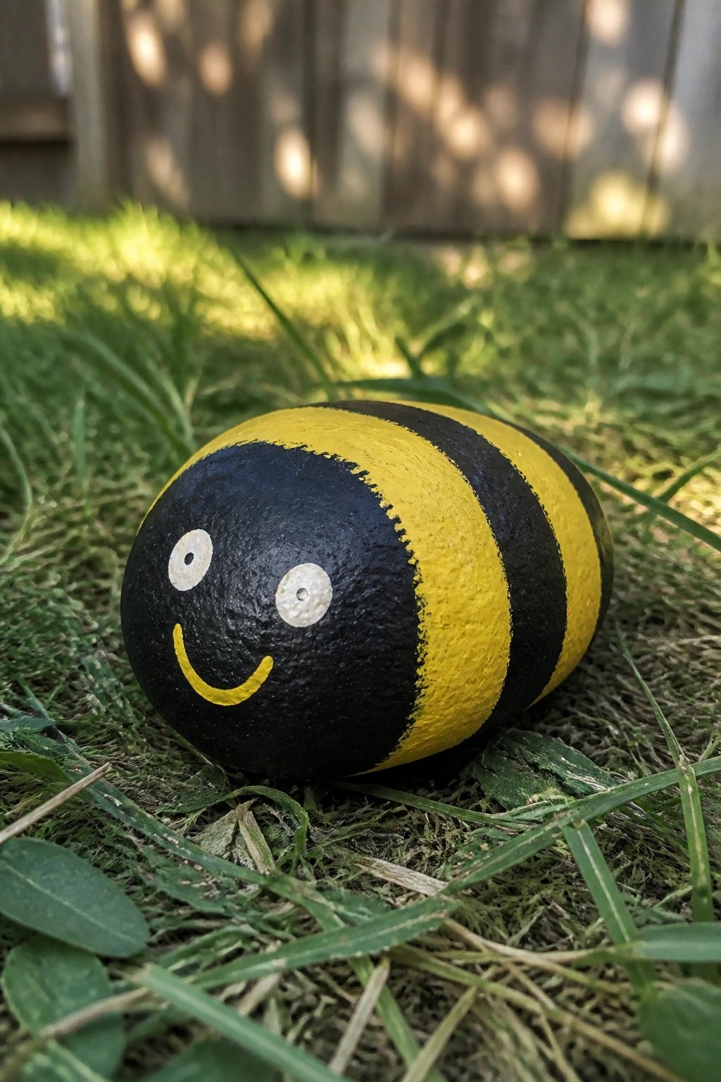 Painted rock bumblebee with black-yellow stripes and smiling face on grass