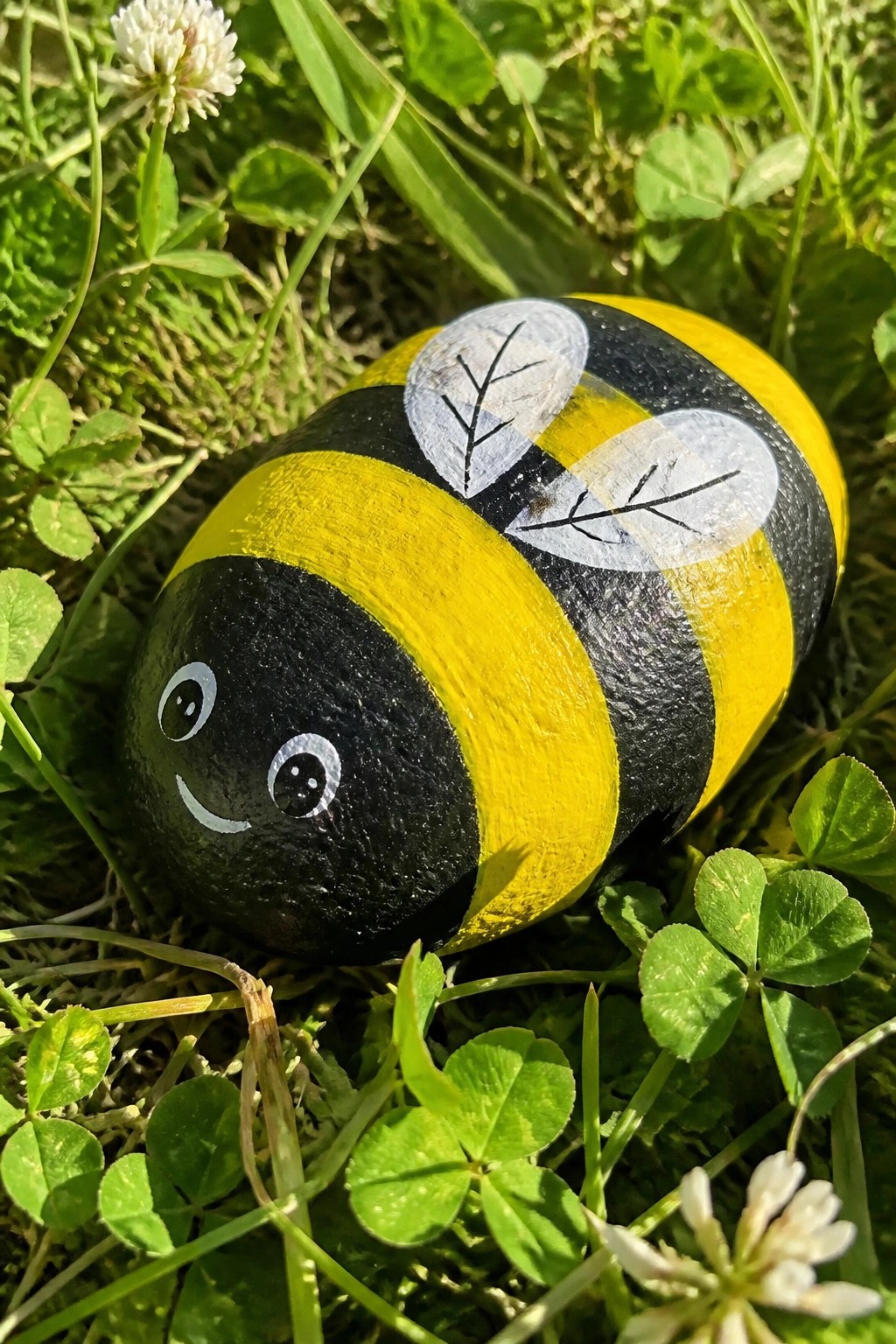 Smiling bumblebee painted on rock with black-yellow stripes and leaf wings in grass