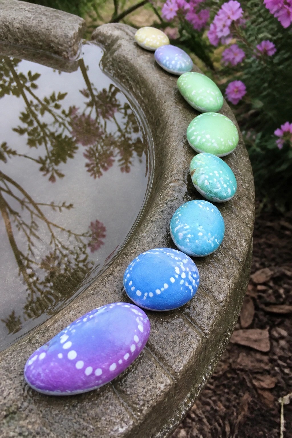Row of gradient-painted stones with white dots on a stone birdbath edge