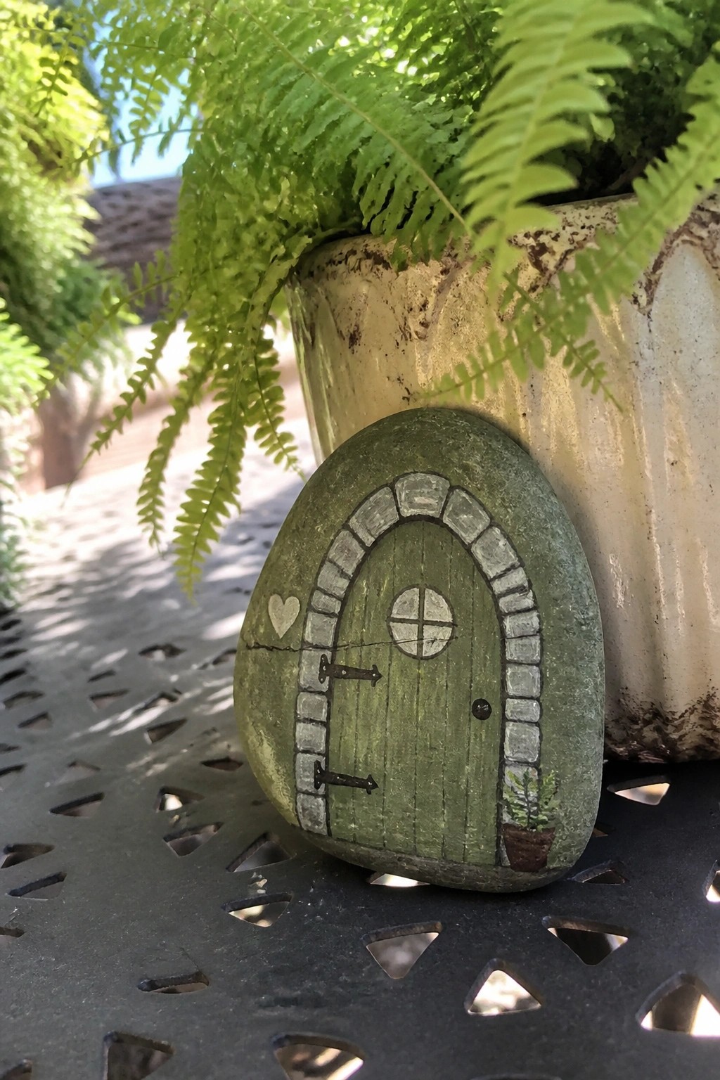 Green rock painted as fairy door with stone arch, hinges, window, and plant