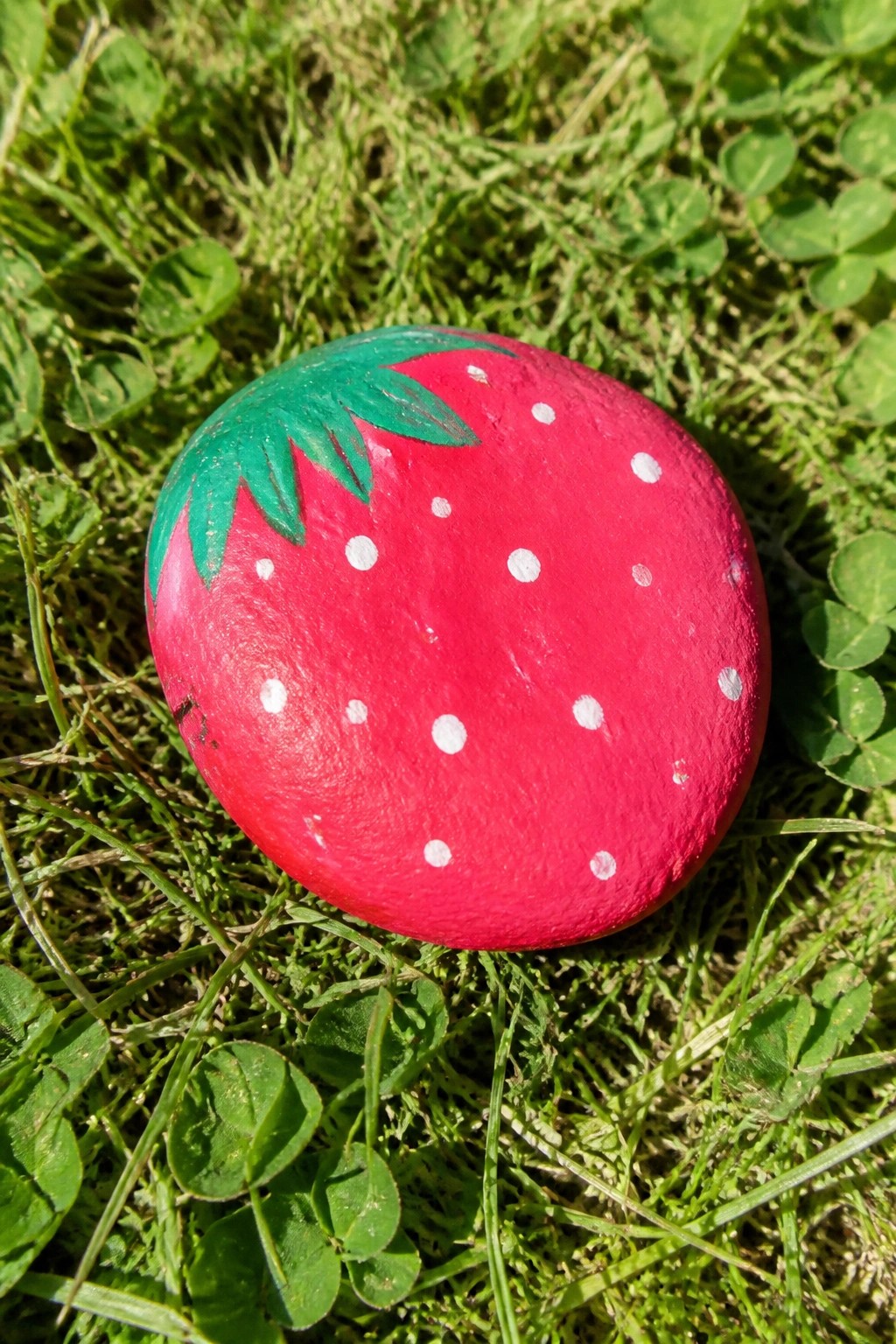 A red painted rock with white dots and green leaves on top sits on green grass.