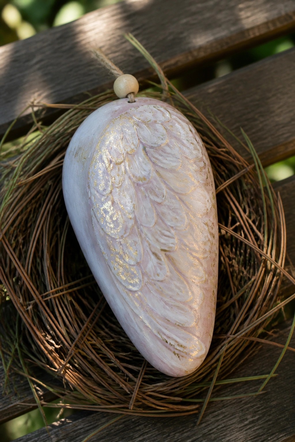 Pink egg-shaped ornament with gold embossed wings in a pine needle nest.