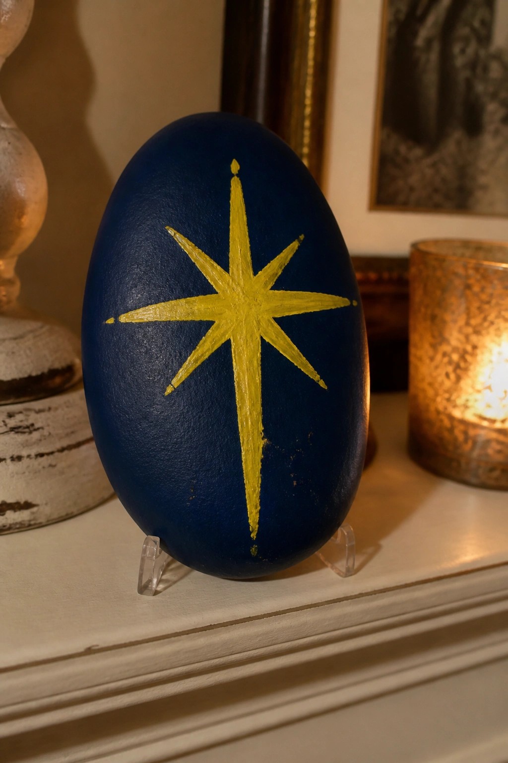Dark blue egg with yellow star on clear stand beside lit candle.