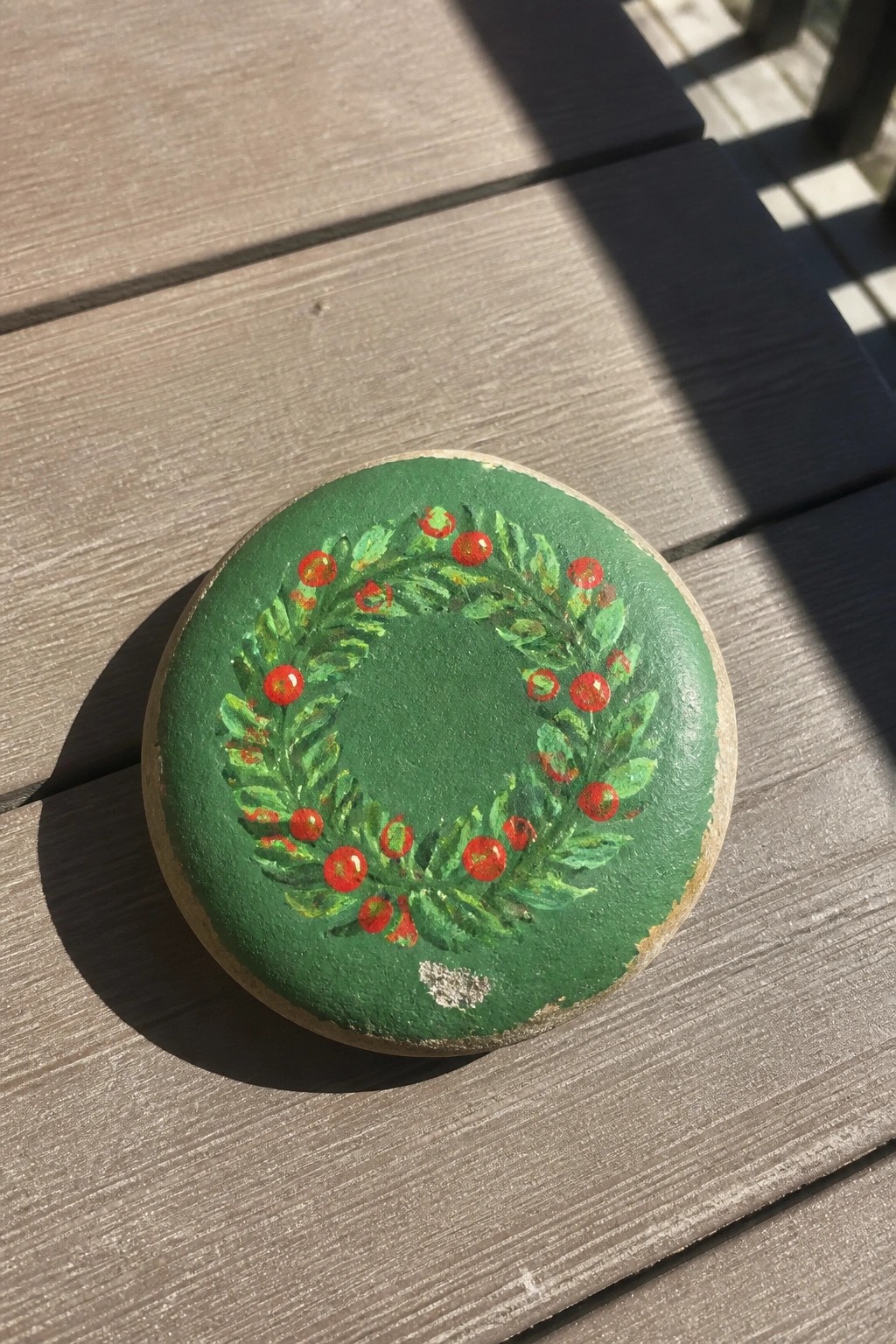 Green painted stone with wreath of leaves and red berries on wood