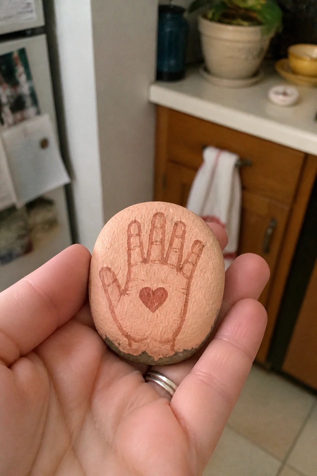 Hand holding a peach-colored stone painted with handprint and heart