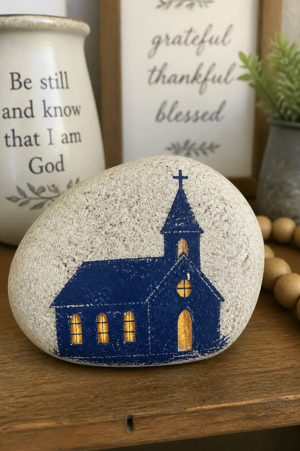 Painted rock with blue church, glowing yellow windows, on wooden table