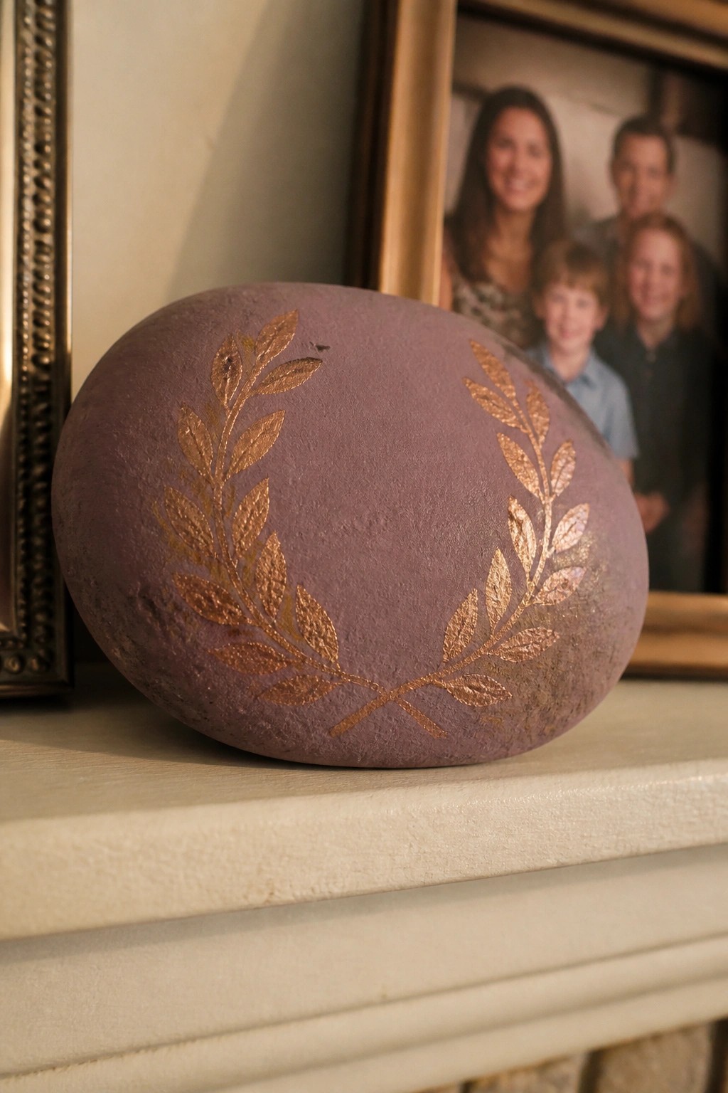 Purple stone with gold laurel branches on white mantel near family photo