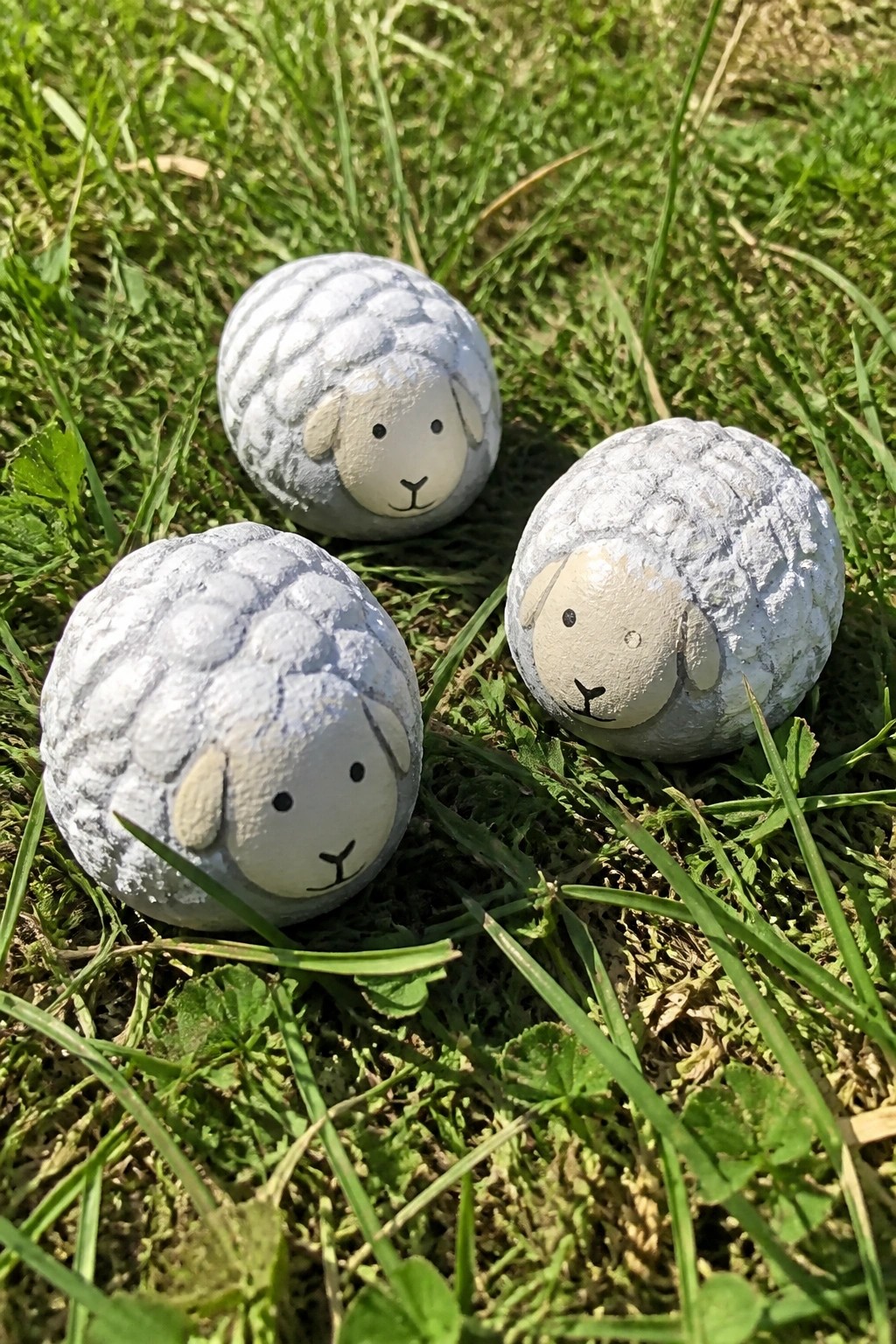 Three painted rocks shaped like sheep with faces on green grass.