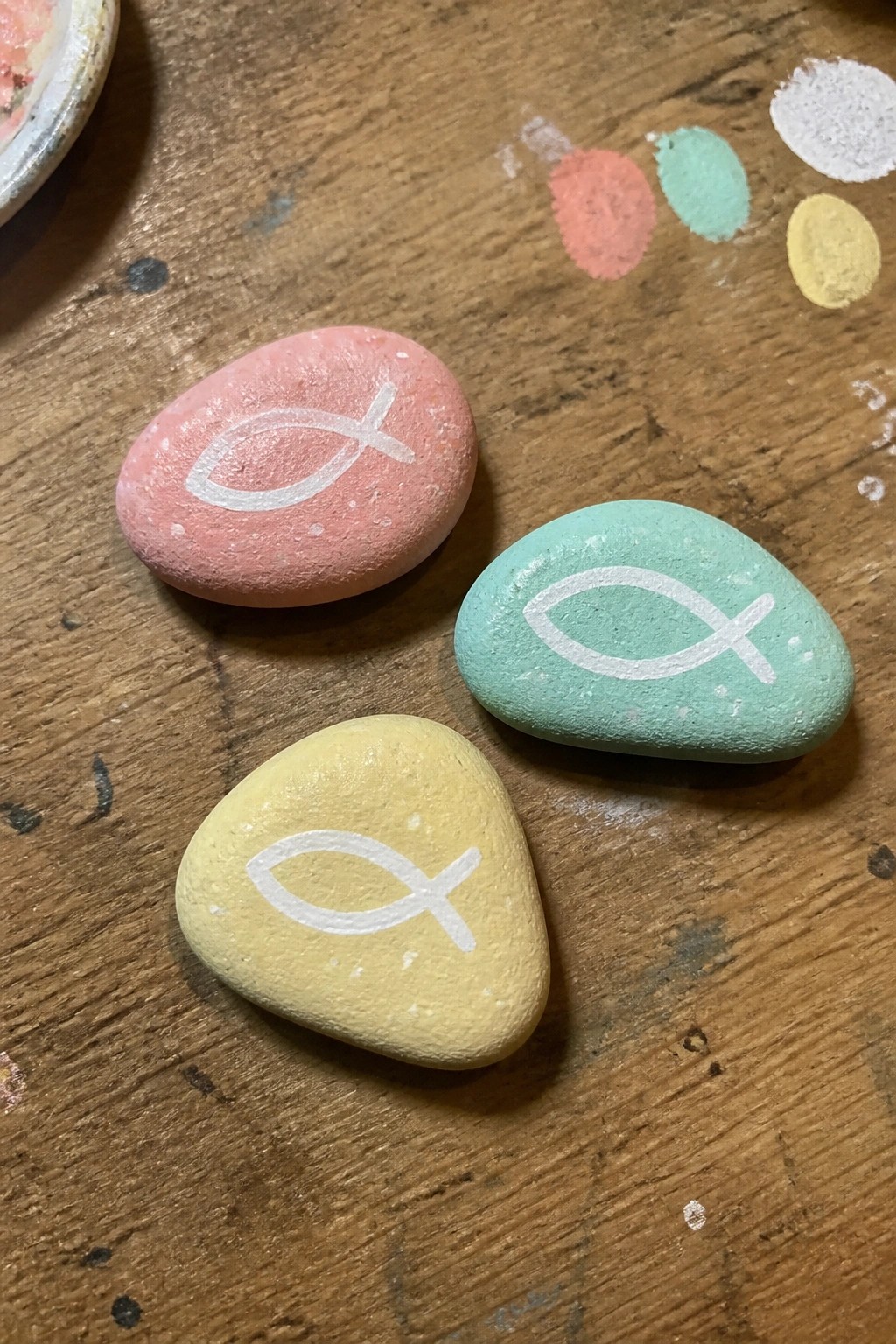 Three pastel rocks in pink, green, and yellow with white fish symbols on wood