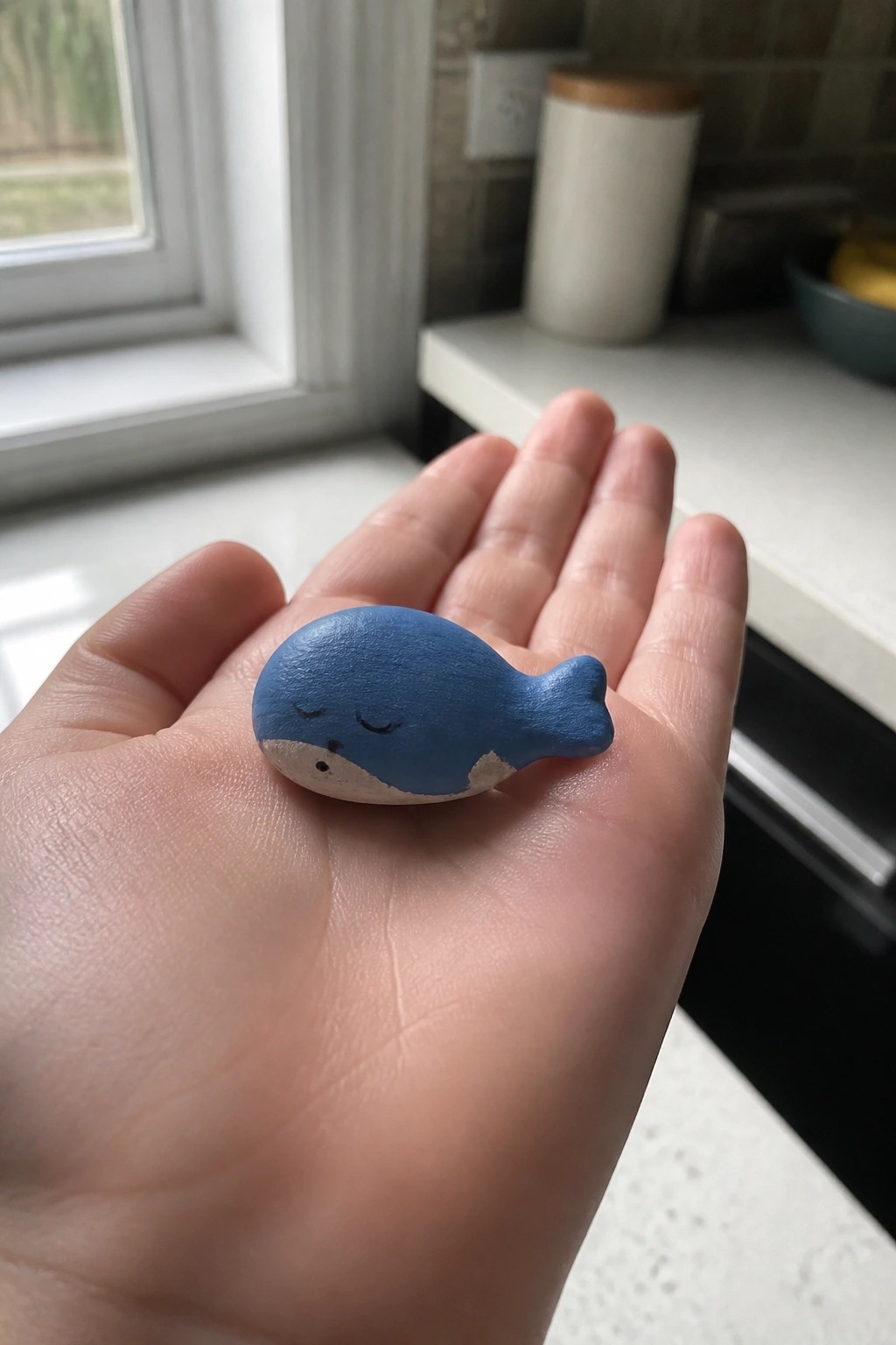 A hand holding a small blue wooden whale with a painted smiling face.